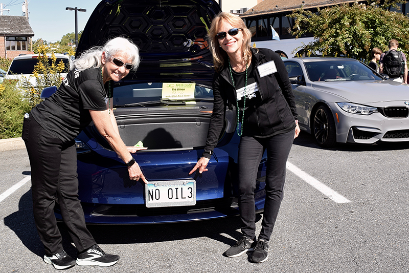 Elvia Thompson & Lynne Forsman point to a No Oil license plate at Annapolis NDEW Kick Gas EV Showcase Sept 2021